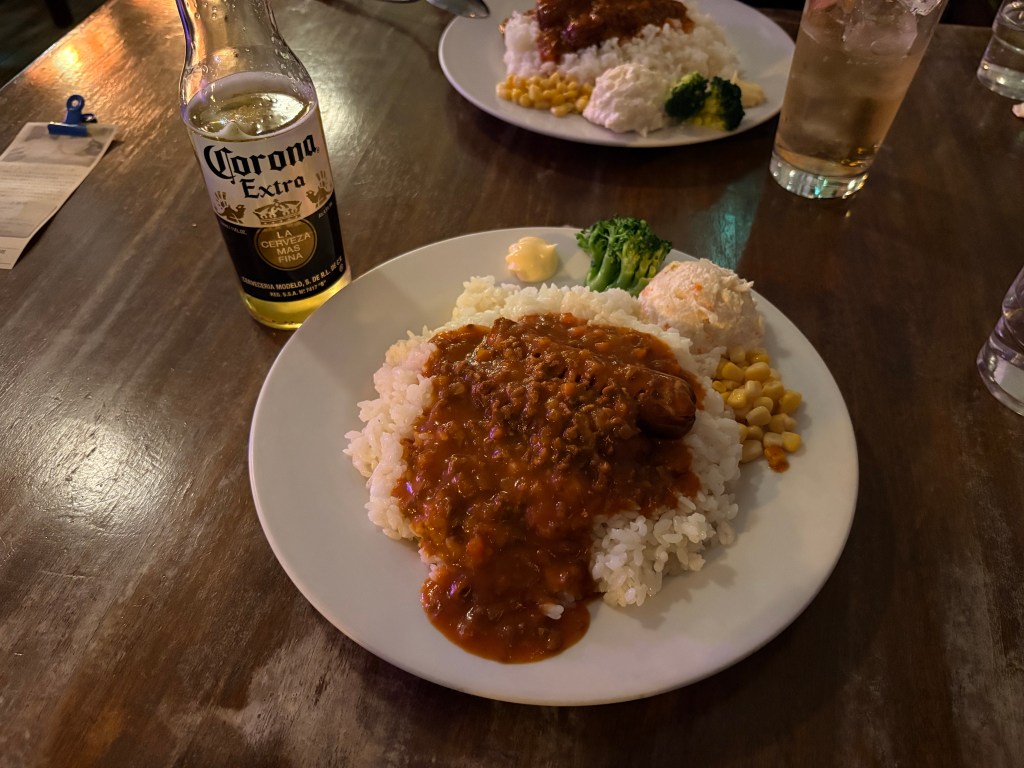 A plate of Cisco Rice consisting of buttered rice, sausages, and meat sauce, served with a bottle of Corona Extra on a wooden table.