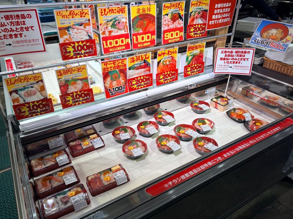 A display case of various seafood bowls with salmon, roe, and crab, with price tags around 1,100 yen.