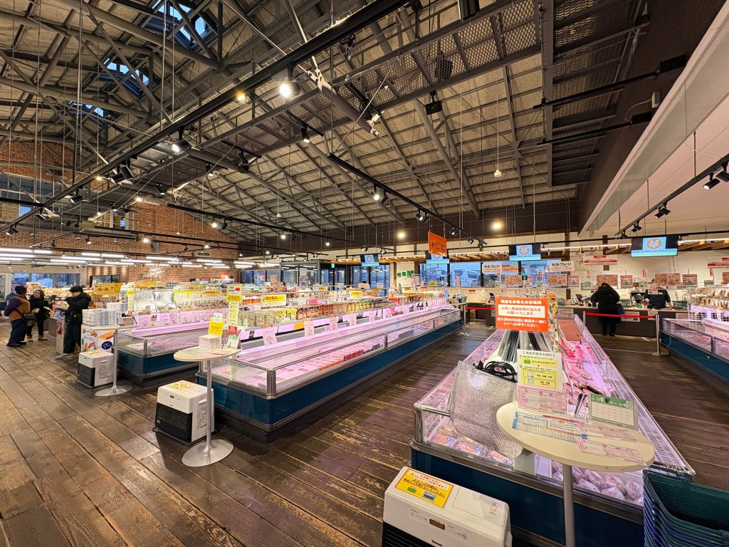 A large, open-concept market interior with high wooden ceilings and neat rows of refrigerated display cases.