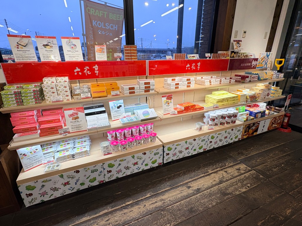 A wooden display shelf showcasing colorful floral-patterned boxes of Rokkatei sweets.