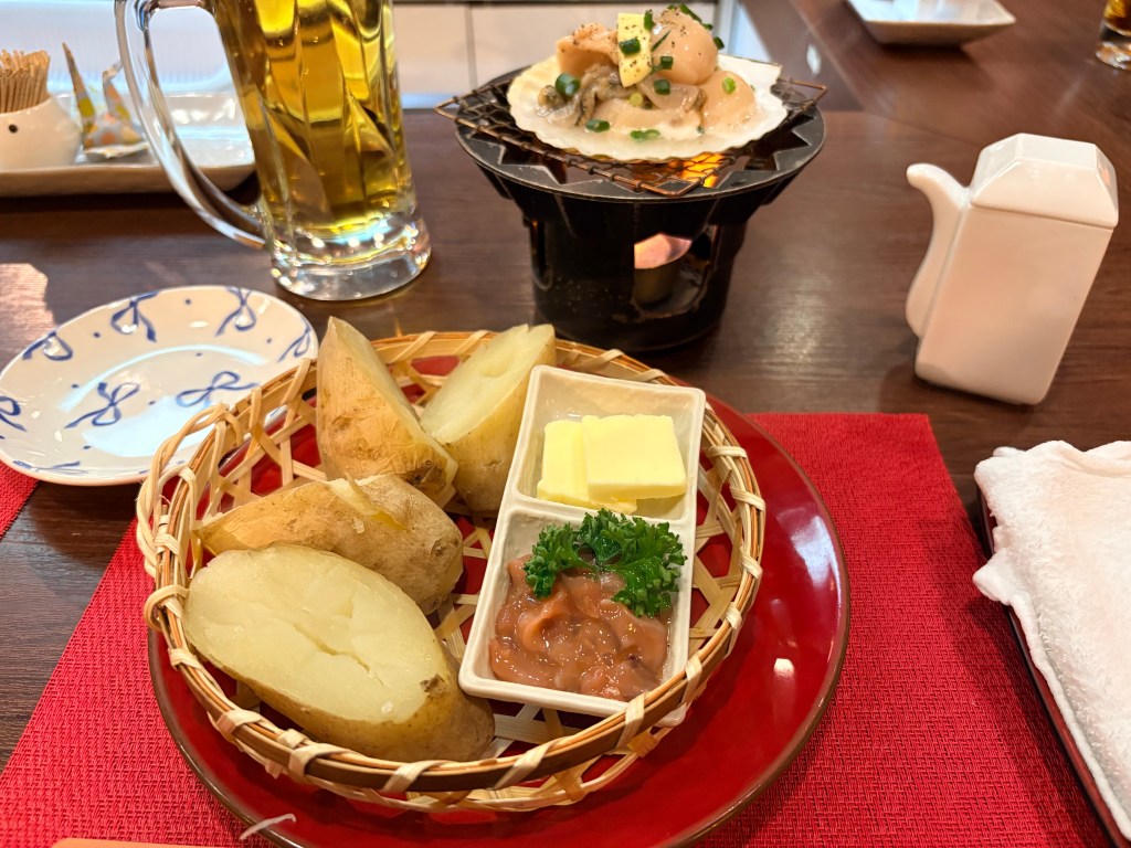 A basket of steamed potatoes served with two pats of butter and a generous side of dark, salted fermented squid.