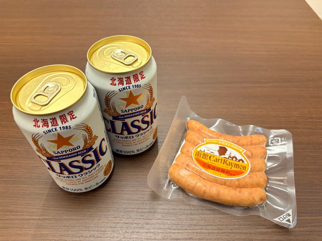 Two cans of Sapporo Classic beer and a pack of Carl Raymon sausages on a table.