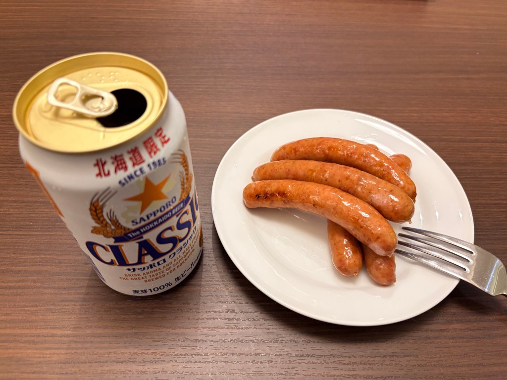 Four golden-brown grilled sausages served on a white plate next to a can of beer.