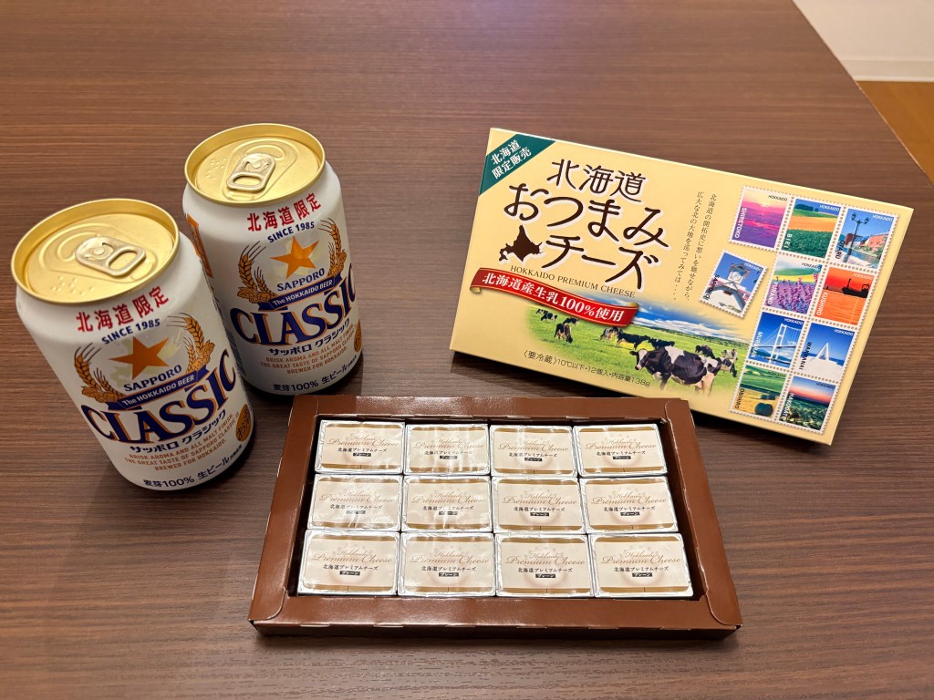 An open box of Hokkaido Premium Cheese showing 12 individually foil-wrapped pieces next to beer cans.