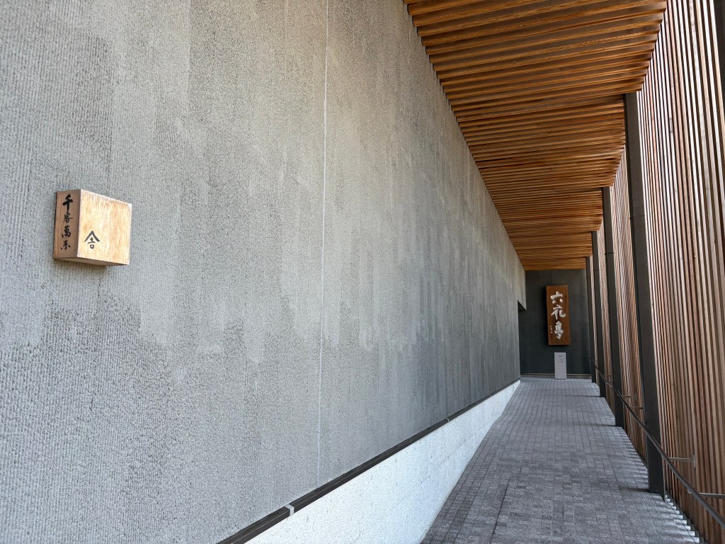 A long, sophisticated entrance walkway at Rokkatei, featuring a beautiful wooden louvered ceiling and stone pavement.