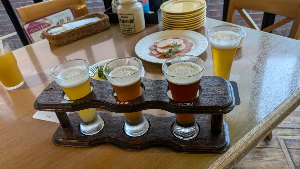 A tasting flight of three distinct Hakodate craft beers served in a wooden holder.