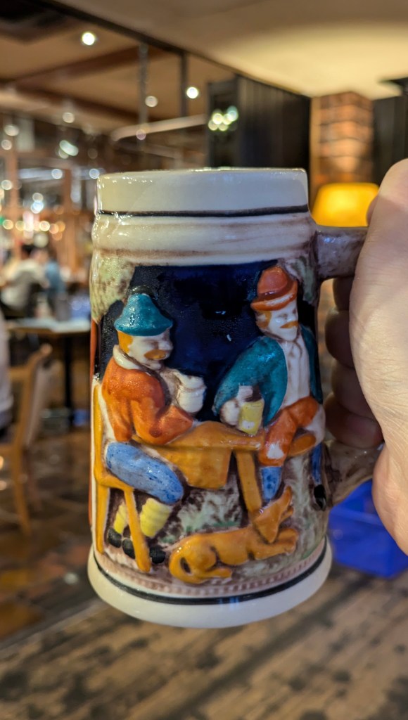 A large, ornate ceramic beer mug with traditional embossed patterns held in hand.