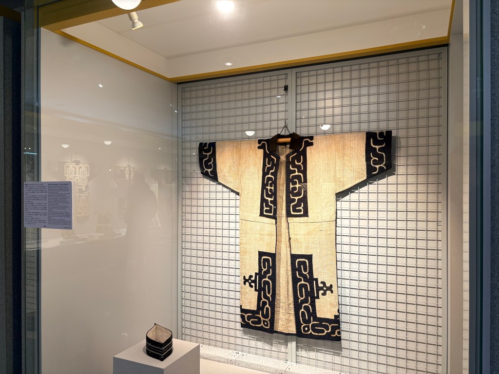 Traditional Ainu robes with geometric patterns and an English info plaque.