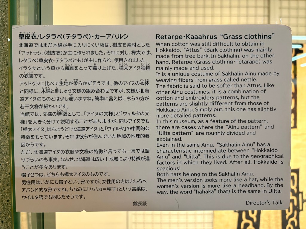 Traditional Ainu robes with geometric patterns and an English info plaque.