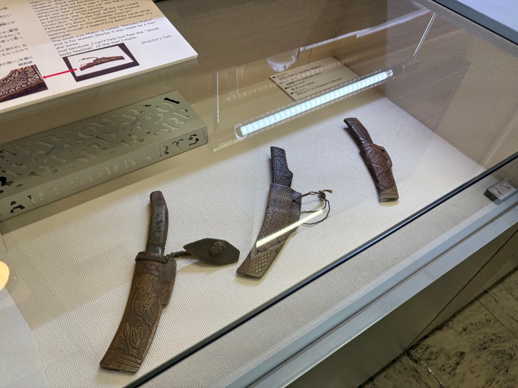 Three traditional Ainu knives with intricately carved wooden sheaths.