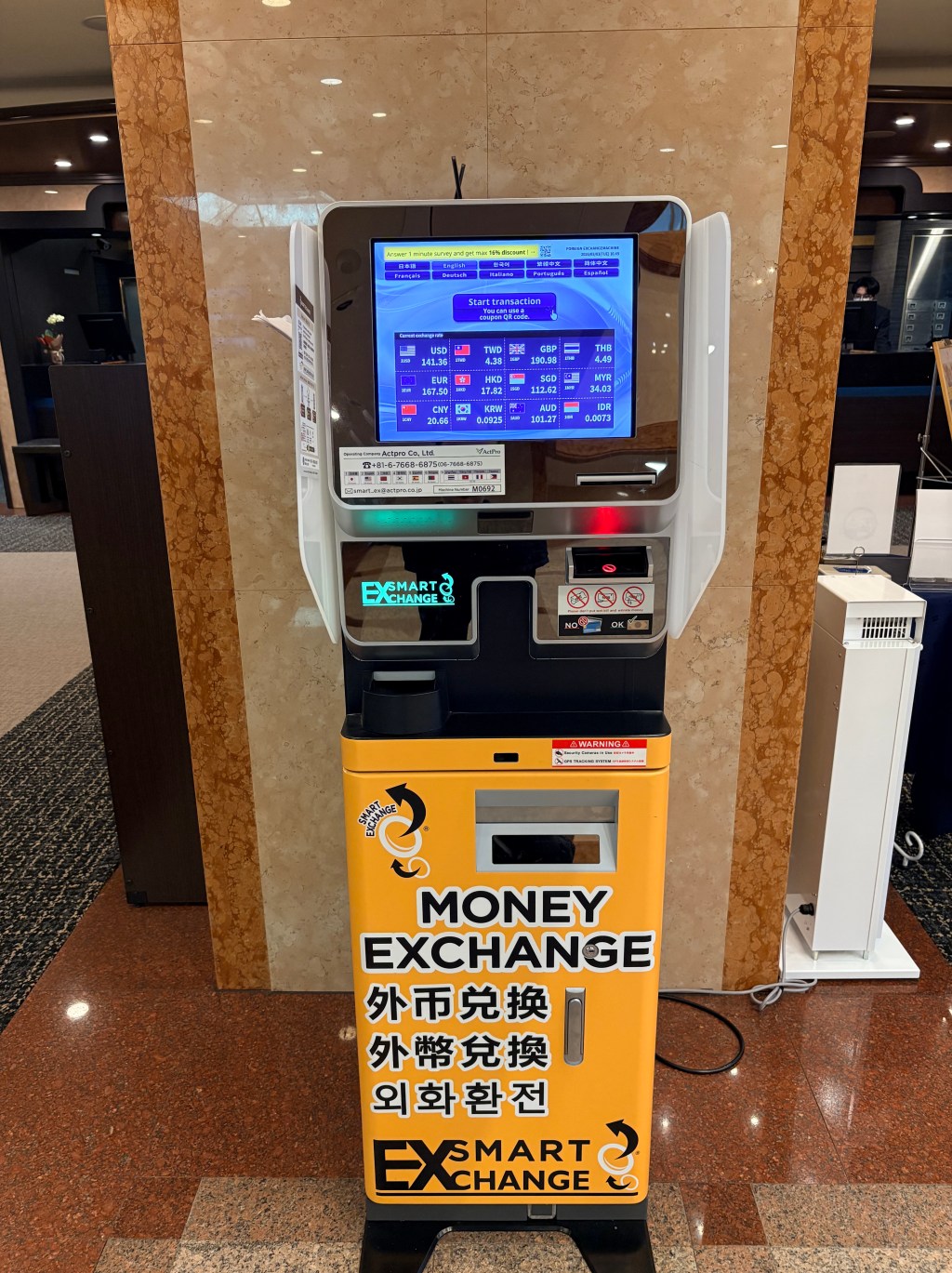 A yellow automated currency exchange machine located in a hotel lobby.