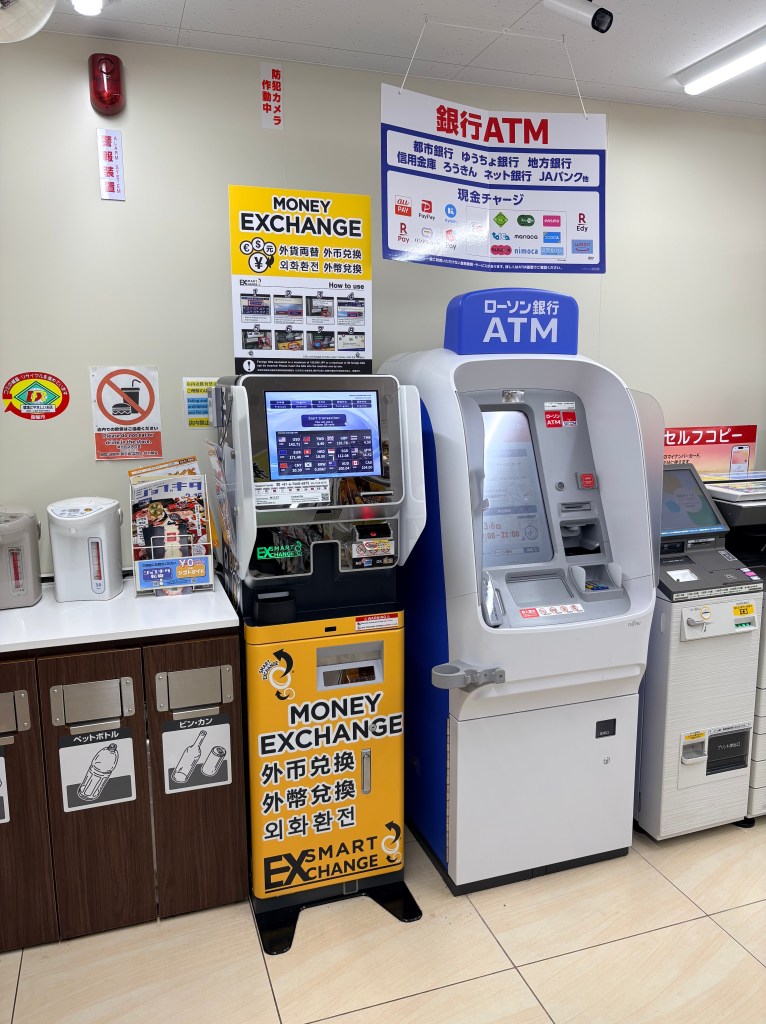 A currency exchange machine standing next to an ATM inside a Lawson convenience store.