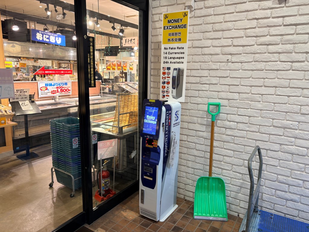 A slim currency exchange machine located near the entrance of a seafood market.