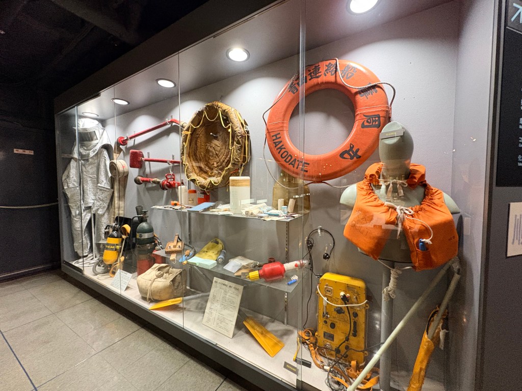 A display case featuring a large orange lifebuoy, life jackets, firefighting suits, and other rescue equipment.