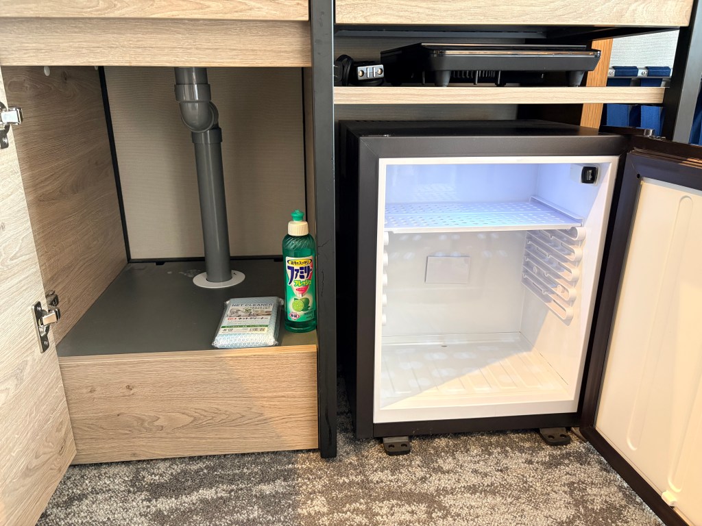 A detailed shot of the kitchenette counter showing a built-in single-burner induction (IH) cooktop next to a small stainless steel sink with a modern faucet.