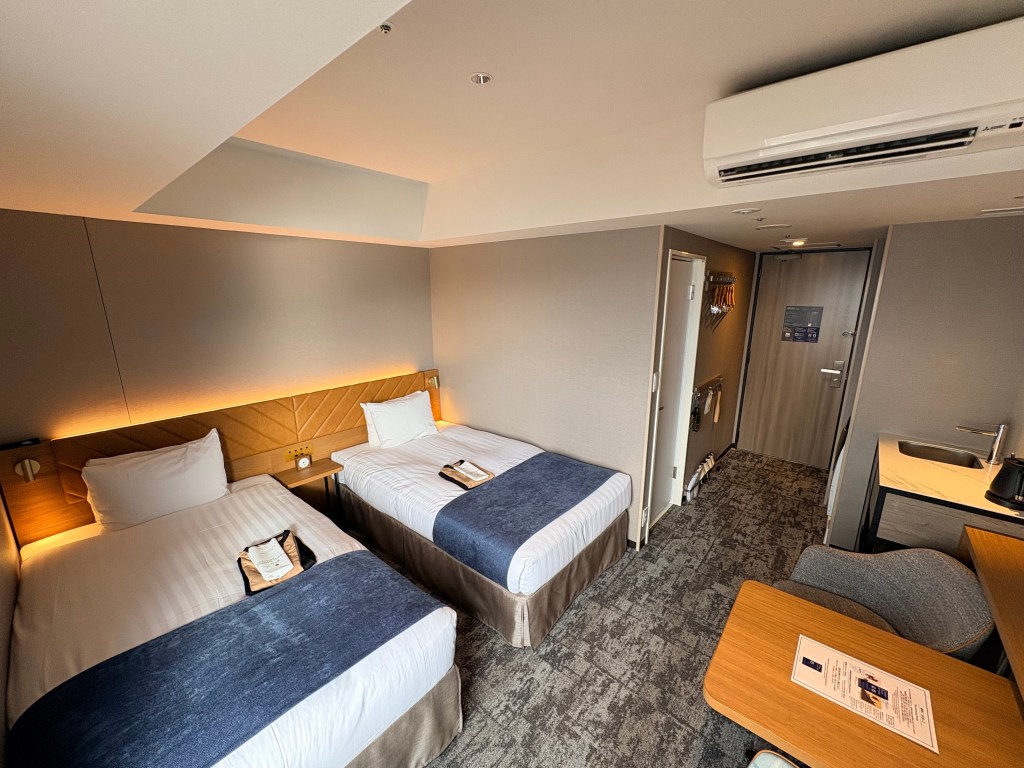 An overhead view of the twin room showing the arrangement of the beds, the small dining table, and the entrance hallway.