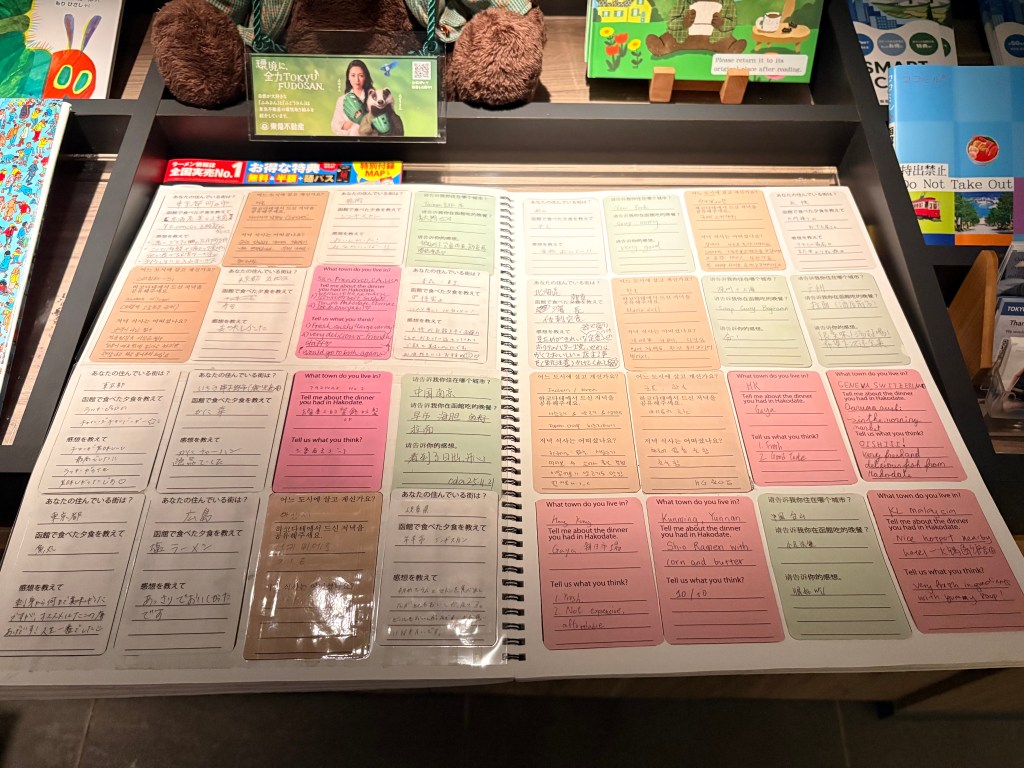 A close-up shot of an open spiral notebook in the lobby, containing rows of colorful cards with handwritten restaurant reviews in various languages.