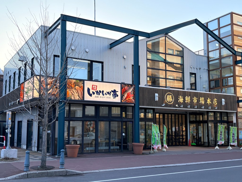 Exterior view of the modern Hakodate Kaisen Ichiba building with large signs for the market and Ika-ika Tei restaurant.