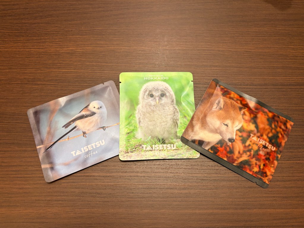 Three colorful coffee drip bags with photos of a Long-tailed tit bird, a baby owl, and a Shiba Inu dog.