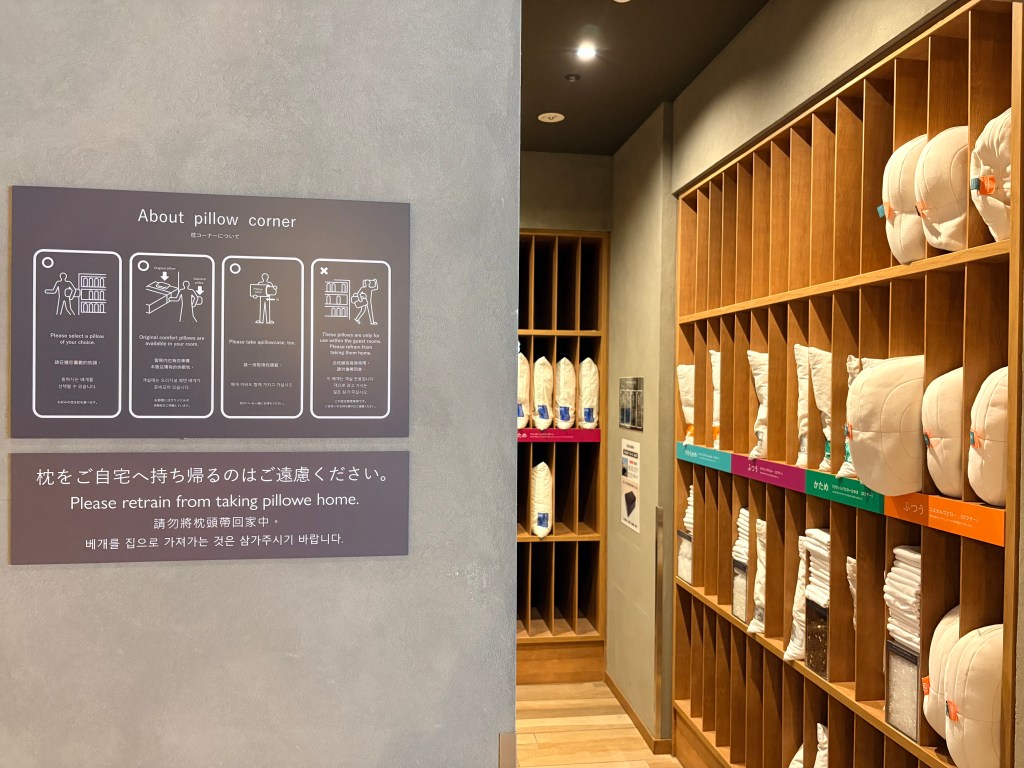 A photograph of the hotel's pillow bar, showing a wall of wooden cubbies filled with various types of pillows and a sign explaining how to choose one.