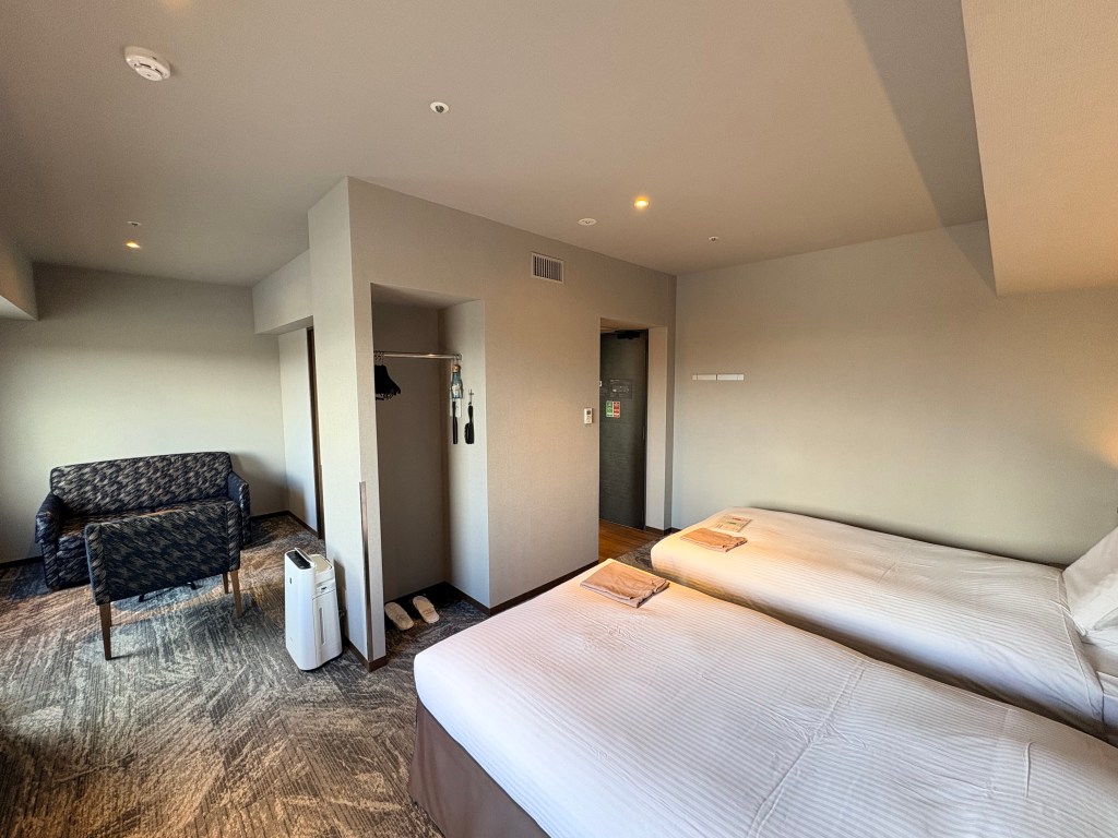 View from inside the hotel room looking towards the entrance door, showing an open closet area with hangers and a full-length mirror.