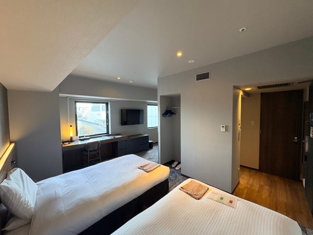 A close-up shot of a desk in a hotel room, featuring a lamp, an information tablet, tissues, and an air purifier on the floor next to it.