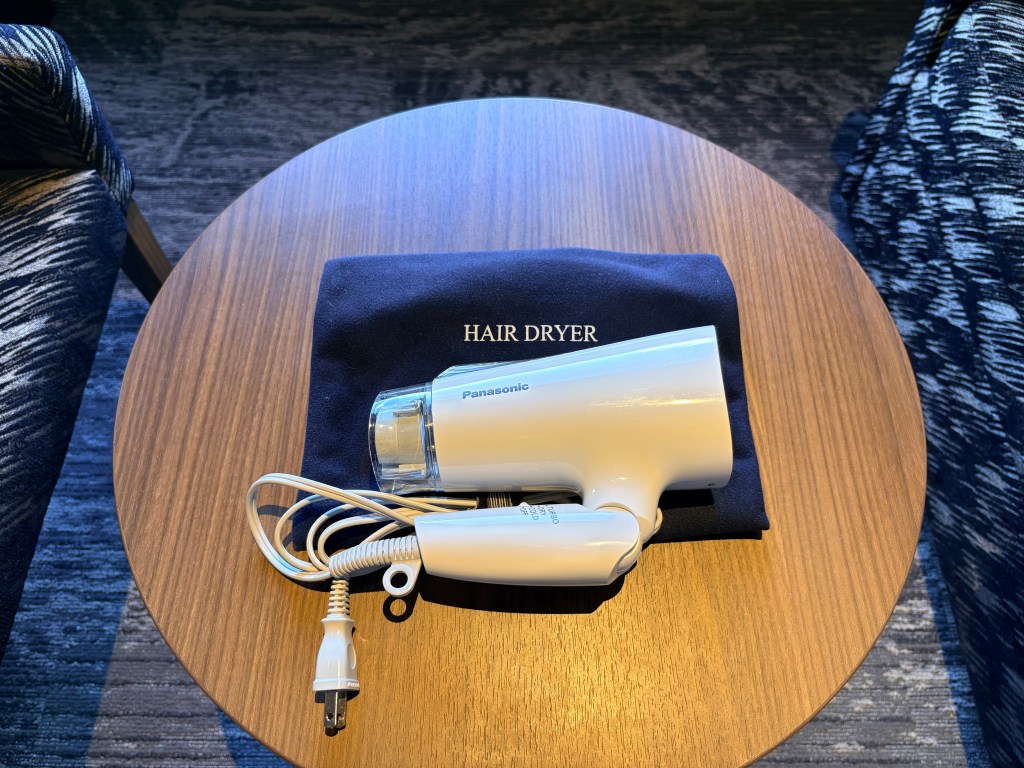A white Panasonic hair dryer resting on its navy blue storage bag on a wooden side table.