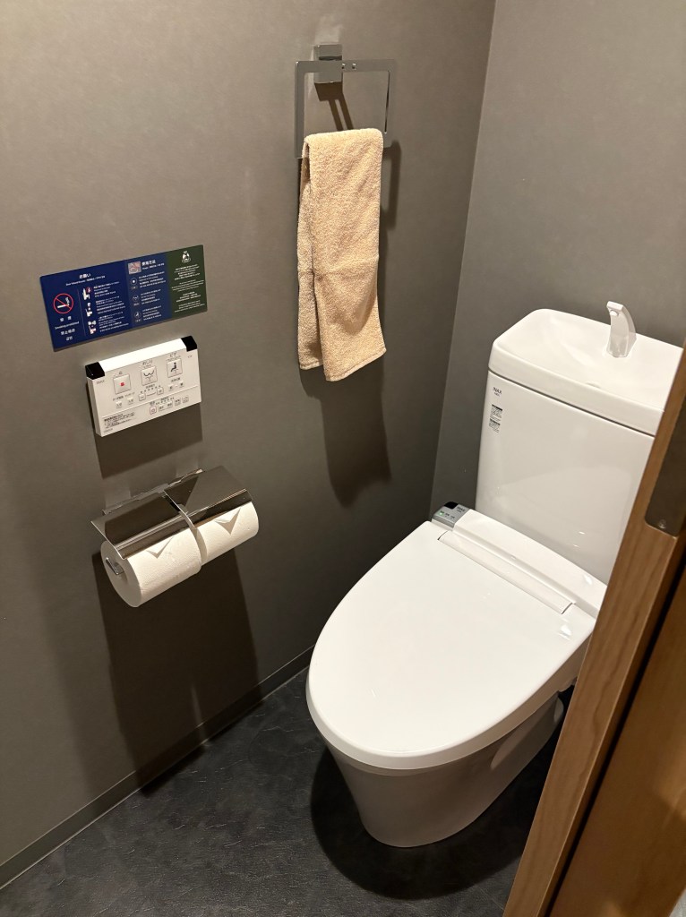 A clean, brightly lit shot of a modern white TOTO toilet and a small sink inside a private restroom.