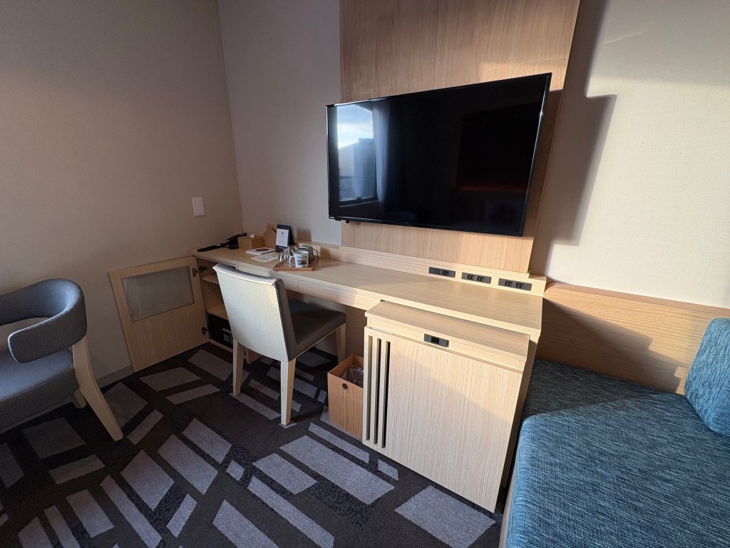 A close-up shot of two small, colorful squid-shaped cushions resting on a white-sheeted hotel bed.