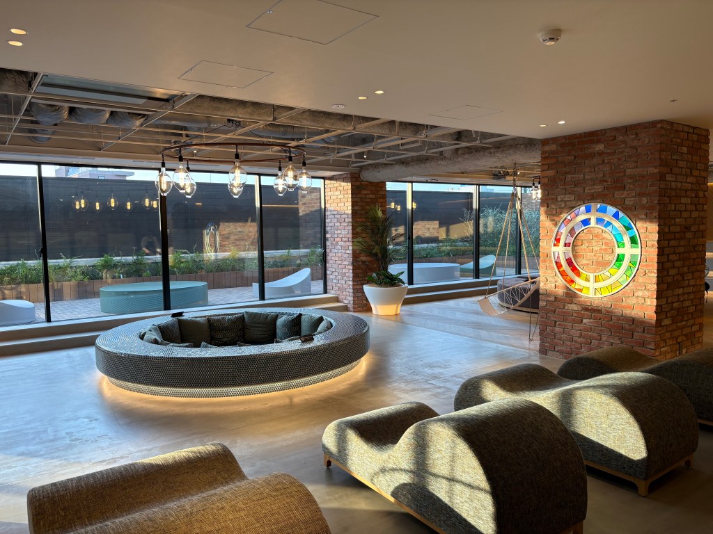 A low-light photograph from inside the lounge, focusing on a wooden counter bar area with various bottles and glasses, perfect for an evening drink.