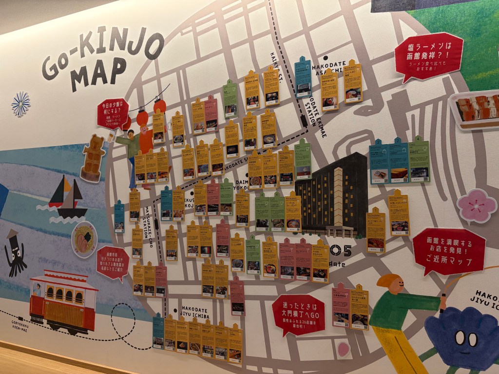 A close-up shot of the Go-KINJO Map, focusing on colorful informational cards written in both Japanese and English, describing various local restaurants and attractions.