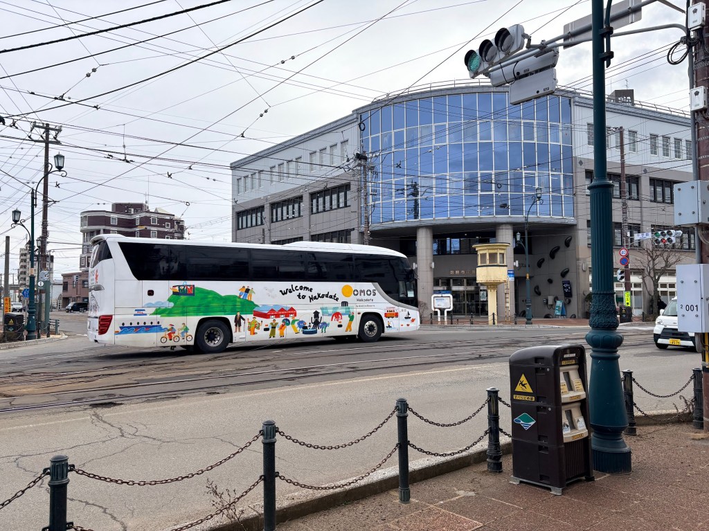 A daytime photograph of a white shuttle bus with a cute squid illustration and the "OMO FREE BUS" logo, parked at the hotel entrance.