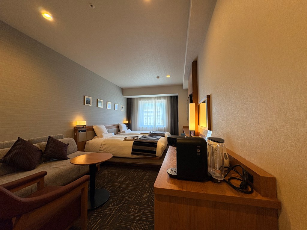 Full view of the Premium Japanese Twin room at Hakodate Kokusai Hotel, featuring twin beds on a raised tatami platform and a seating area with a sofa.