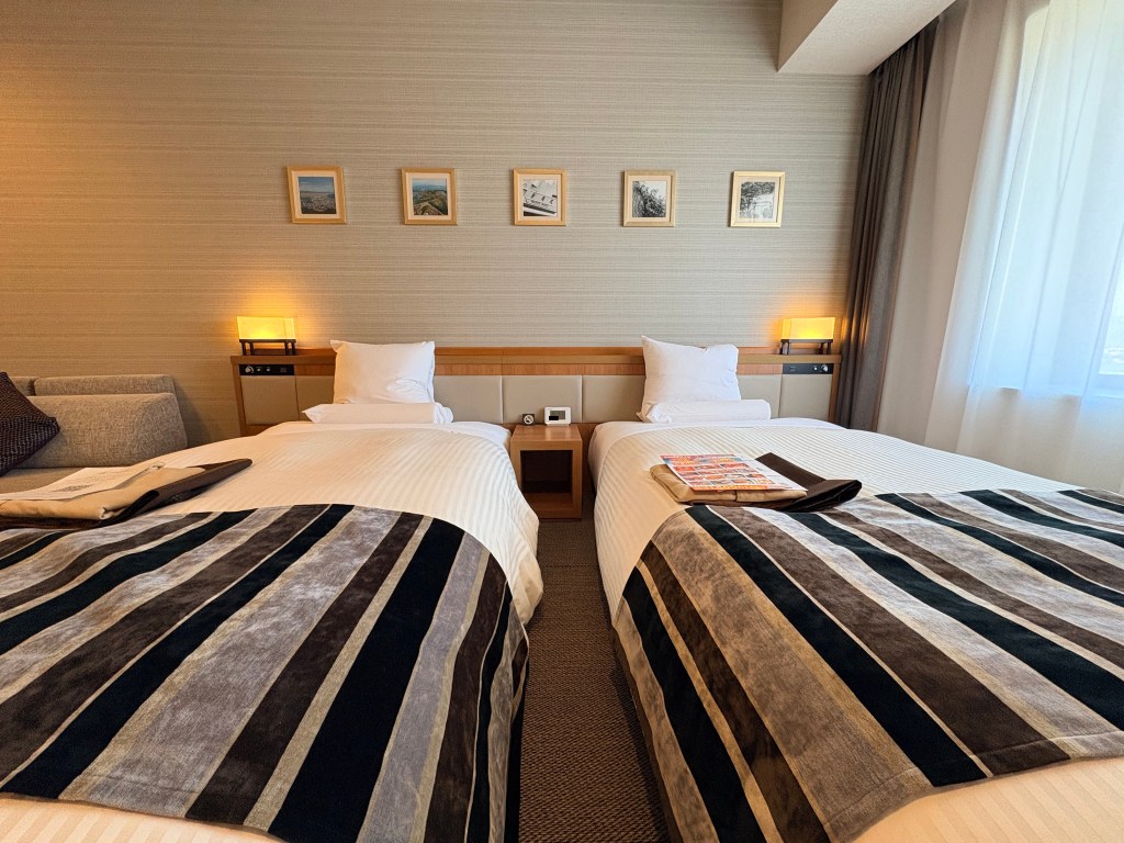 Close-up view of the two twin beds fitted with striped bed runners and headboard lamps in the Premium Japanese Twin room.