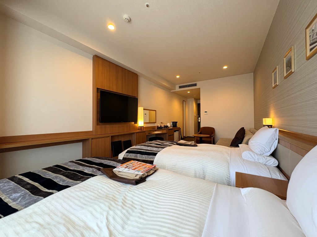 Perspective looking toward the wall-mounted TV and entryway from beside the twin beds in the Premium Japanese Twin room.